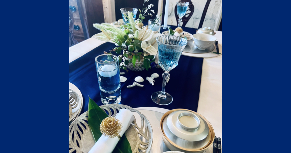 久高島イシキ浜の神話の世界を再現した、風水空間デザイン®によるテーブルコーディネート。アクアブルーのクロスに珊瑚や白壺、五穀の象徴を設えた、祈りと清めの精神の聖域を創り出す食卓の演出。